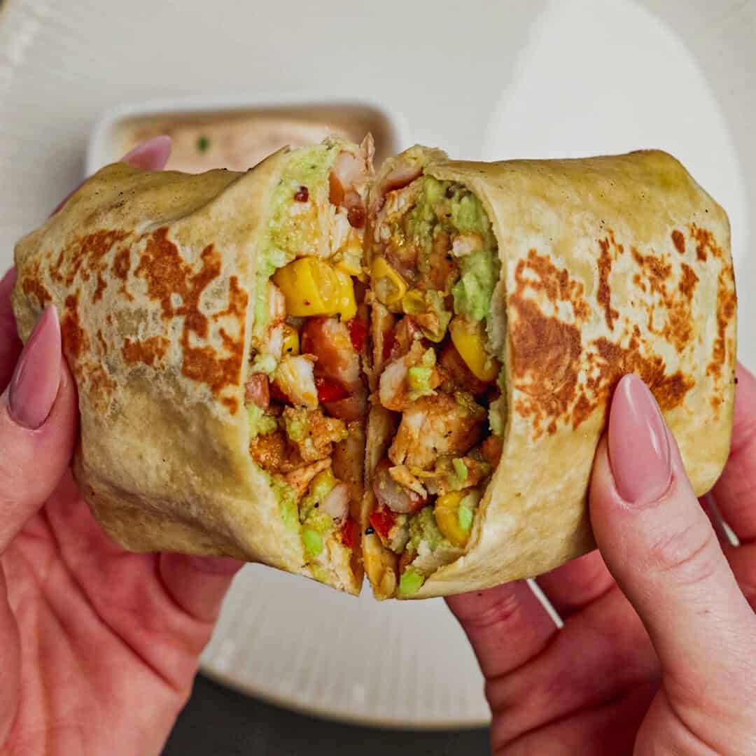 Svež burrito s sestavinami, pripravljeno za uživanje, v roki na mizi.